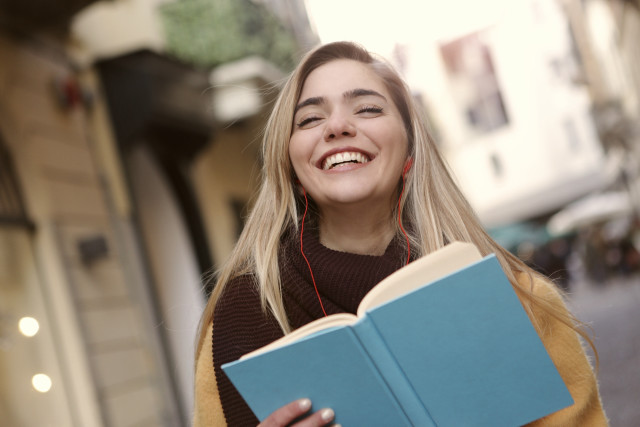 Woman smiling holding book headphones free wallpaper - medium preview image