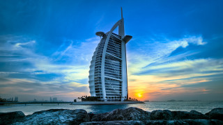 Tall building rocky beach ocean - a boat in the background free wallpaper