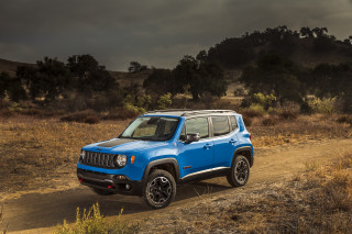 Blue jeep driving dirt road - a dark sky in the background free wallpaper