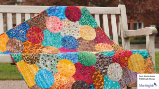 Colorful quilt wooden bench park - a tree in the background and a building in the background free wallpaper