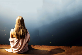 Woman sitting ledge water mountains - her back free wallpaper