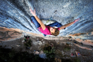 Woman climbing rock face outstretched - her arm free wallpaper