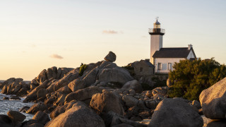 Lighthouse rocky shore dawn mountains - a house in the background free wallpaper