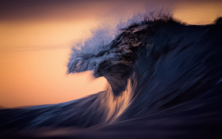 Large wave crashing shore sunset - a yellow sky in the background free wallpaper