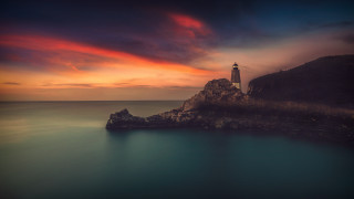 Lighthouse rocky outcrop ocean sunset - a red sky in the background free wallpaper
