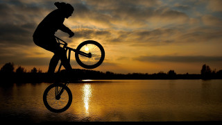 Sunset bike over lake backlighting - the sun in the background free wallpaper