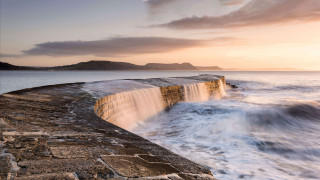 Wave crash stone wall sunset - a mountain in the distance free wallpaper