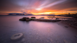 Sunset water rocks boat cloudy - the foreground and a boat in the distance free wallpaper
