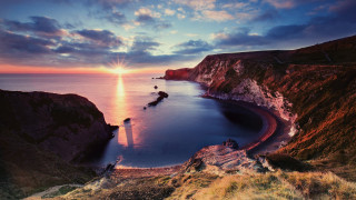 Sunset lake cliff lighthouse rocks - a sunset over a body of water free wallpaper