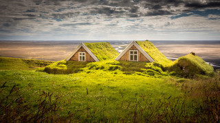 Two houses grass roof hill - a cloudy sky above them free wallpaper