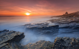 Rocky beach lighthouse sunset foggy - a lighthouse in the distance free wallpaper