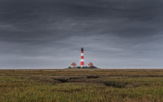 Lighthouse grassy island cloudy sky - a dark sky in the background free wallpaper