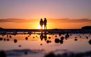 Beach sunset couple silhouette bokeh - the sun setting behind them free wallpaper