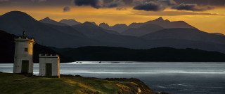 Lighthouse hill overlooking water mountains - rich moody colour free wallpaper