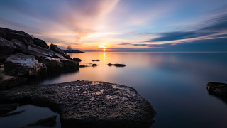 Sunset water rocks clouds horizon - a sunset over a body of water free wallpaper