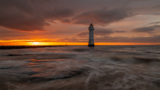 Lighthouse ocean sunset cloudy sky - a body of water below free wallpaper