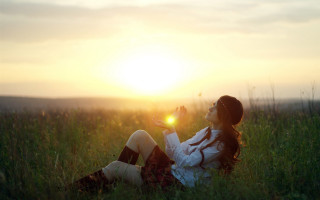 Woman sitting field sunset flare - the sun setting behind her free wallpaper