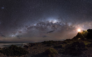 Night sky stars lighthouse rocky - a body of water below free wallpaper