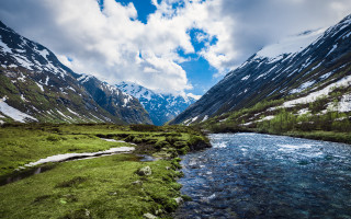 Lush green valley mountains snowy - a lush green valley under a cloudy sky free wallpaper