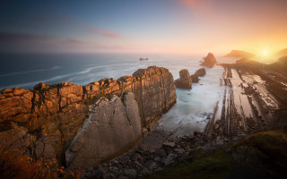 Rocky cliff water sunset mountains - the foreground and a sunset in the background free wallpaper
