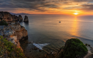 Boat sunset rockycliff lake cloudscape - a boat in the distance free wallpaper