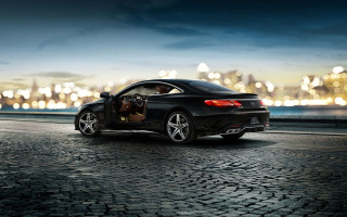 Black car cobblestone city night - a city skyline in the background free wallpaper