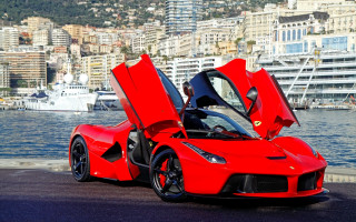 Red sports car waterfront cityscape - a city in the background and a boat free wallpaper