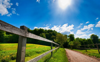 Dirt road fence sunny day - a bright sun in the background free wallpaper
