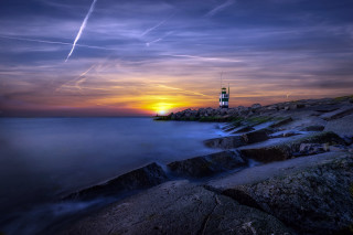 Lighthouse rocky shore sunset contrails - a body of water below free wallpaper