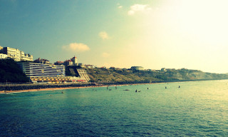 Beach large building people swimming - a hill in the background free wallpaper