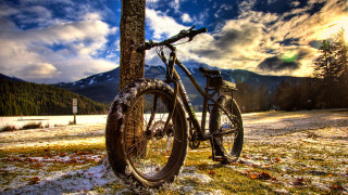 Bicycle parked tree snow mountains - the background and a lake in the foreground free wallpaper