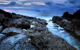Rocky shore water cloudy sky - a small island in the distance free wallpaper